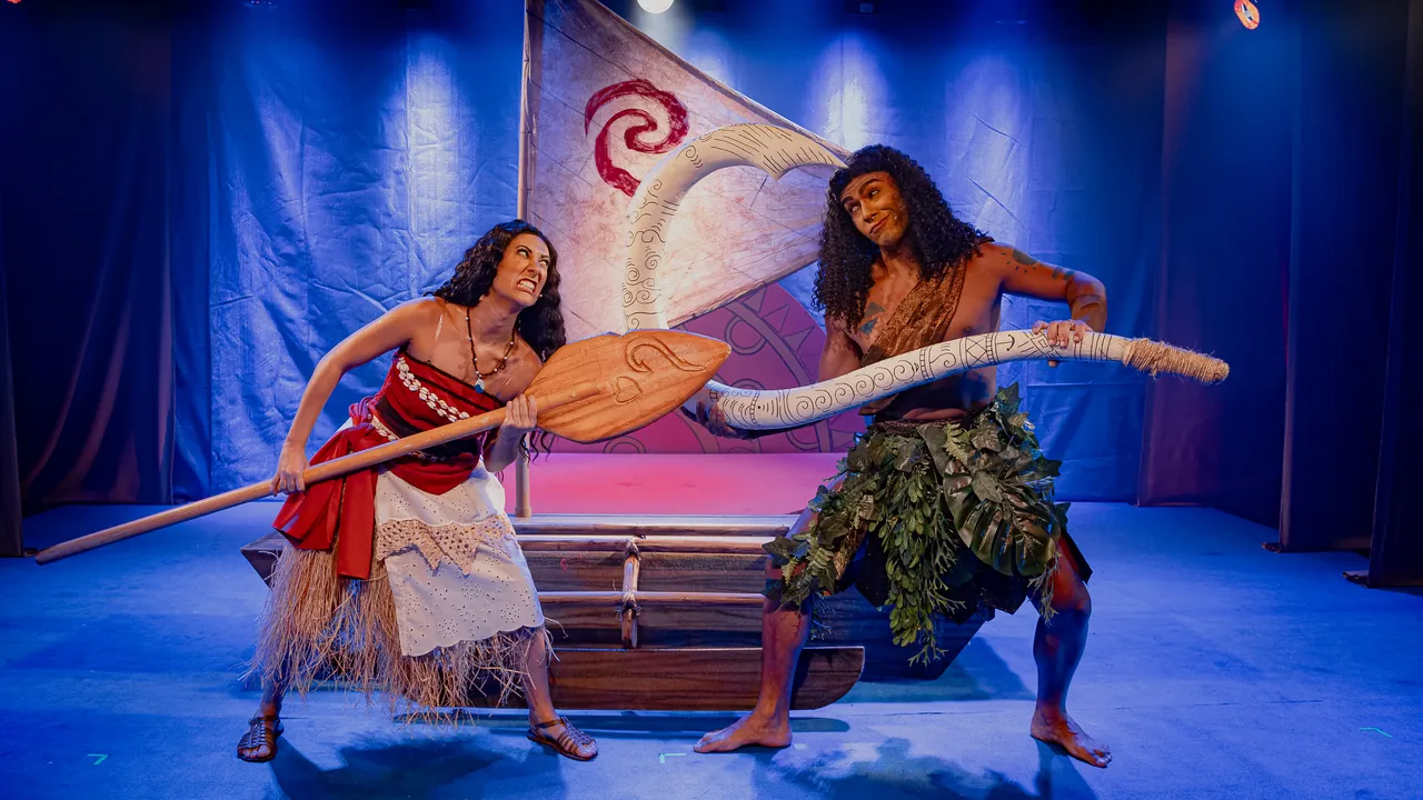 Cena do musical Moana, com duas atrizes no palco segurando um remo diante de uma vela